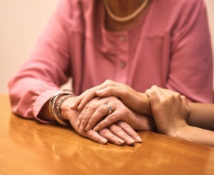 Comfort, love and hands of people on table for empathy, compassion and support in hope together. Home, trust and women with gesture of solidarity on desk for kindness, understanding and forgiveness